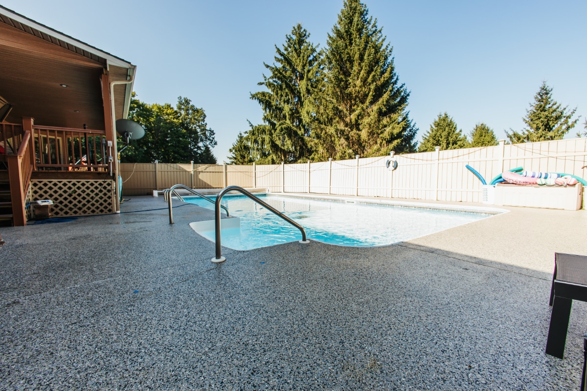 Residential pool with coated concrete deck, handrail, and wood deck surround